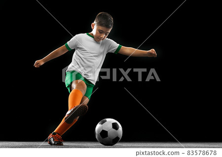 Full-length portrait of boy, child, football player in uniform training isolated over black background. 83578678