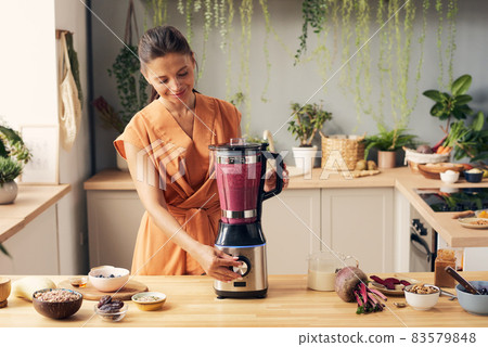Young female pressing start button of blender while cooking 83579848