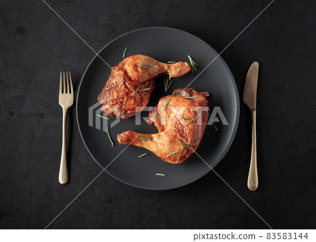 Grilled chicken leg sprinkled with rosemary on a black plate. Grilled chicken leg sprinkled with rosemary on a black plate. 83583144