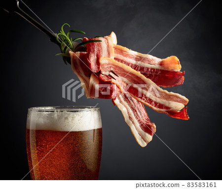 Beer and slices of fried bacon on a fork. 83583161