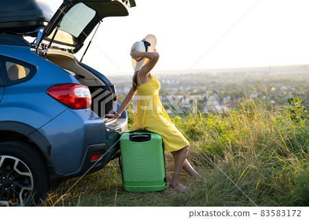 Young woman resting on a green suitcase near her car in summer nature. Travel and vacations concept. 83583172