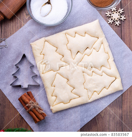 Cutting the dough for Christmas tree shaped puff pastry cookies with sugar and cinnamon, square Cutting the dough for Christmas tree shaped puff pastry cookies with sugar and cinnamon, square 83583567