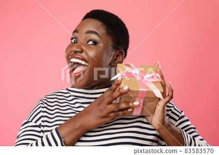 Excited Overweight Black Female Holding Gift Box On Pink Background 83583570