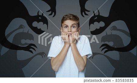 Afraid little boy biting nails in panic, scared of monster shadows on dark background, collage. Mental health concept Afraid little boy biting nails in panic, scared of monster shadows on dark background, collage. Mental health concept 83583835