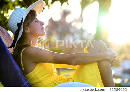 Young woman relaxing outdoors on sunny summer day. Happy lady lying down on comfortable beach chair daydreaming thinking. Calm beautiful smiling girl enjoying fresh air relaxing with closed eyes. Young woman relaxing outdoors on sunny summer day. Happy lady lying down on comfortable beach chair daydreaming thinking. Calm beautiful smiling girl enjoying fresh air relaxing with closed eyes. 83584063