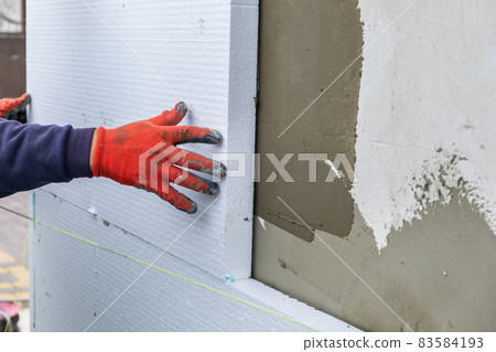 Construction worker installing styrofoam insulation sheets on house facade wall for thermal protection. Construction worker installing styrofoam insulation sheets on house facade wall for thermal protection. 83584193