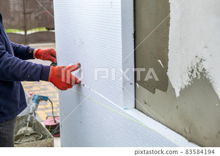 Construction worker installing styrofoam insulation sheets on house facade wall for thermal protection. 83584194