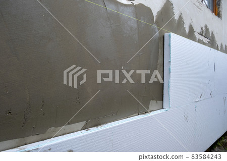 Installation of styrofoam insulation sheets on house facade wall for thermal protection. 83584243
