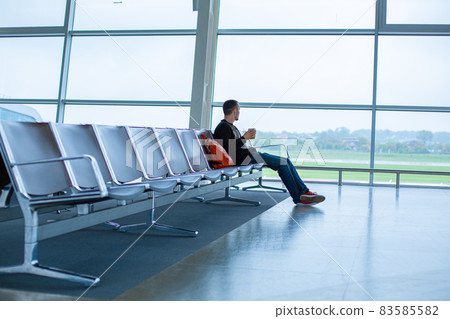A guy is sitting on an empty row of seats in front of a large stained glass window in an airport terminal, waiting for a flight A guy is sitting on an empty row of seats in front of a large stained glass window in an airport terminal, waiting for a flight 83585582