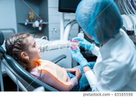 female pediatric dentist orthodontist educating little girl patient using teeth model with brecets. 83585598