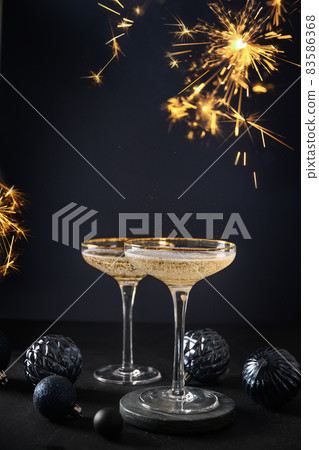 Festive champagne in wine glasses and Christmas blue baubles on dark background. 2022 New Year party Festive champagne in wine glasses and Christmas blue baubles on dark background. 2022 New Year party 83586368