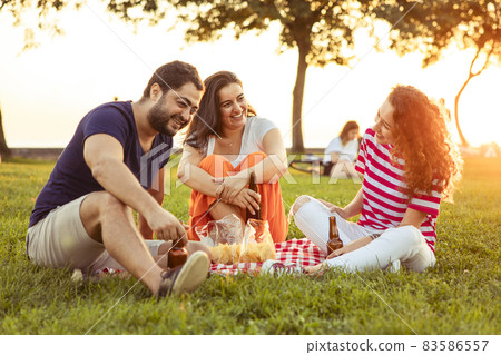 Three friends sitting on the grass in the park Three friends sitting on the grass in the park 83586557