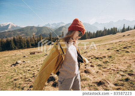 Young blond woman with sunglasses dancing in mountains. Freedom, happiness, travel and vacations concept, outdoor activities. Happy Girl wearing red hat and a yellow jacket. Wind in the hair. Young blond woman with sunglasses dancing in mountains. Freedom, happiness, travel and vacations concept, outdoor activities. Happy Girl wearing red hat and a yellow jacket. Wind in the hair. 83587223