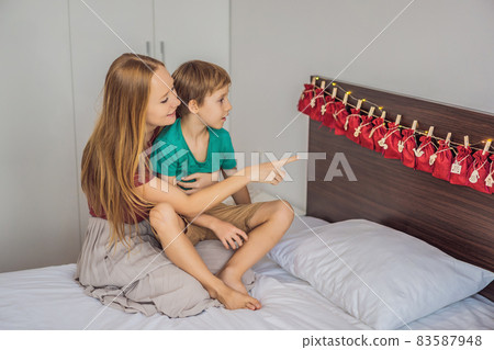 Smiling boy sitting on a bed opening first present from advent calendar. Winter seasonal tradition. Copy space 83587948