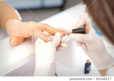 Hands of manicure master in white protective gloves apply polish to female fingernails. Hands of manicure master in white protective gloves apply polish to female fingernails. 83588017