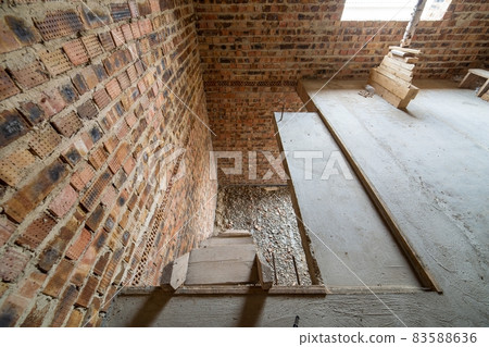 Interior of unfinished brick house with concrete floor and bare walls ready for plastering under construction. Real estate development Interior of unfinished brick house with concrete floor and bare walls ready for plastering under construction. Real estate development 83588636