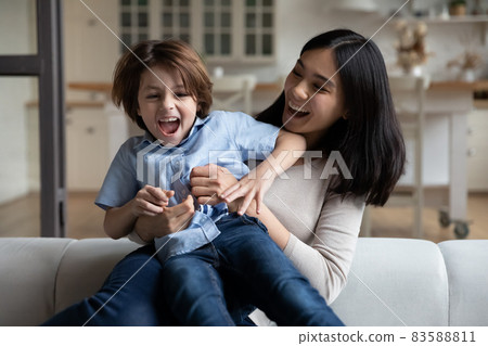 Happy laughing Asian mom tickling excited screaming boy on couch Happy laughing Asian mom tickling excited screaming boy on couch 83588811
