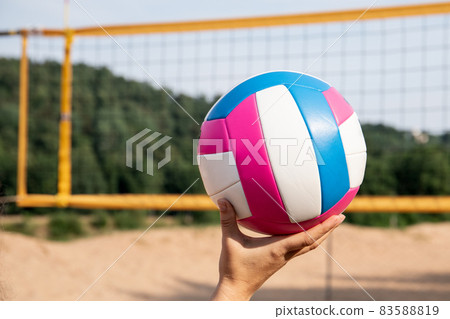 Colorful beach volleyball ball in a woman's hand. Volleyball court and net on the beach 83588819