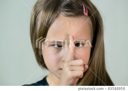Close-up portrait of happy smiling little girl with long hair looking with crossed eyes at her point finger. Close-up portrait of happy smiling little girl with long hair looking with crossed eyes at her point finger. 83588958