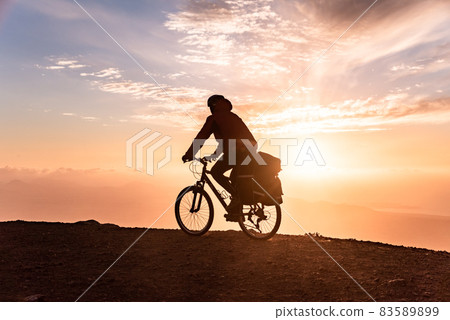 Mountain bicycle rider with backpack travels over sunrise background 83589899