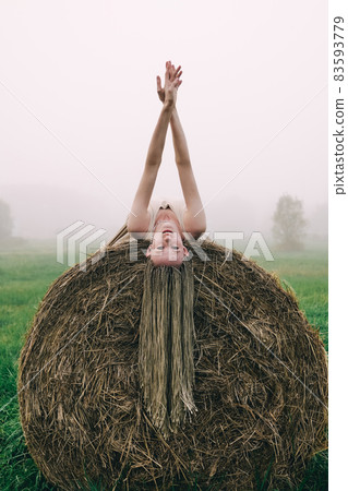 Young woman in beige dress lying on haystacks at twilight time Young woman in beige dress lying on haystacks at twilight time 83593779