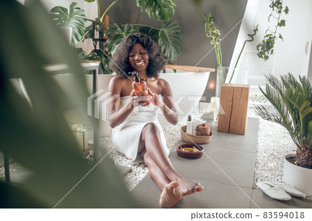 Pretty dark-skinned woman civered with towel choosing body lotion 83594018