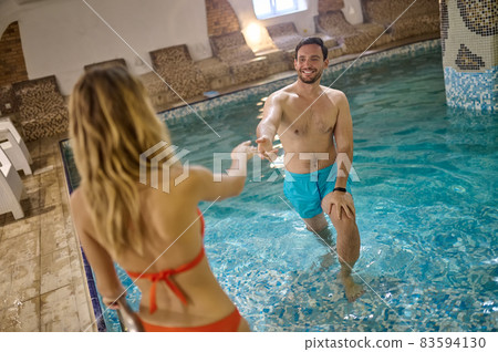A couple in a pool holding hands and looking at each other 83594130