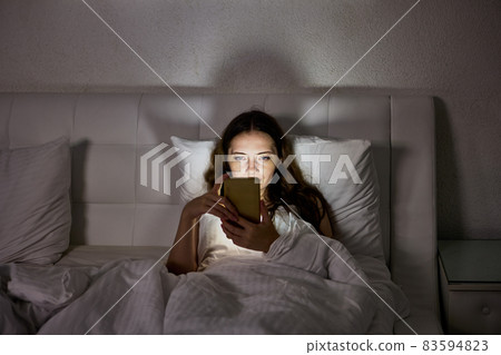 Light from screen of phone on woman face in bed. Light from screen of phone on woman face in bed. 83594823