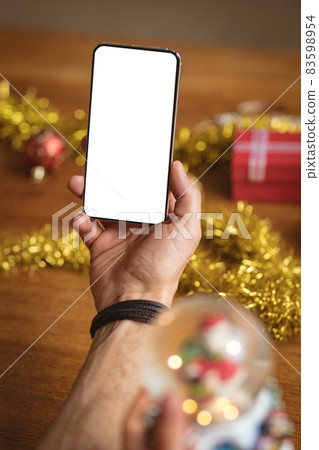 Hand holding smartphone with copy space against christmas gifts and decorations on wooden table Hand holding smartphone with copy space against christmas gifts and decorations on wooden table 83598954