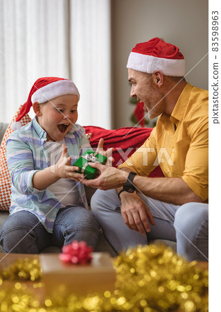Caucasian father giving a christmas gift to his son at home during christmas Caucasian father giving a christmas gift to his son at home during christmas 83598963