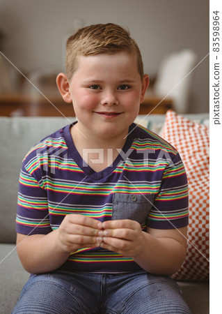 Portrait of caucasian boy making hand gestures sitting on the couch at home 83598964