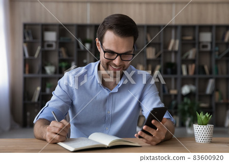 Happy young business man writing notes using cellphone. Happy young business man writing notes using cellphone. 83600920