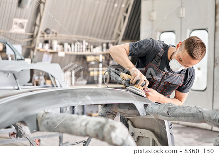 The mechanic works with a grinding tool. Sanding of car elements. Painting car service. Repairing car section after the accident. 83601130