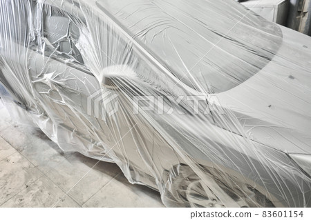 Garage painting car service. section of the car is covered with primer. vehicle is covered with protective paper. Repairing car body work after the accident by working sanding primer before painting. Garage painting car service. section of the car is covered with primer. vehicle is covered with protective paper. Repairing car body work after the accident by working sanding primer before painting. 83601154