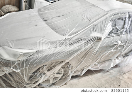 Garage painting car service. section of the car is covered with primer. vehicle is covered with protective paper. Repairing car body work after the accident by working sanding primer before painting. Garage painting car service. section of the car is covered with primer. vehicle is covered with protective paper. Repairing car body work after the accident by working sanding primer before painting. 83601155