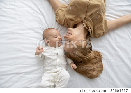 Top view loving young mother and baby lying on bed Top view loving young mother and baby lying on bed 83601517