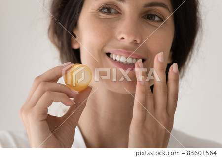 Closeup young beautiful woman holding jar apply balm on lips Closeup young beautiful woman holding jar apply balm on lips 83601564