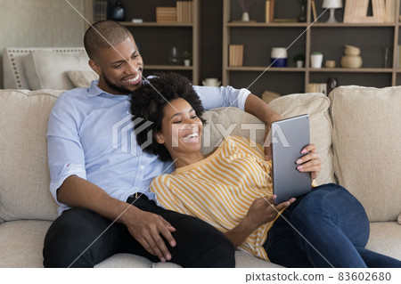 Relaxed smiling millennial mixed race couple using tablet. Relaxed smiling millennial mixed race couple using tablet. 83602680