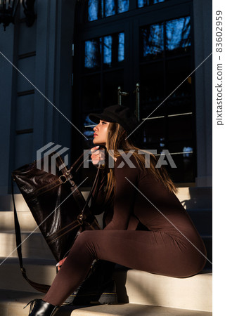 Fashionable young brunette woman with long legs wearing Solid Long Sleeve Bodycon One Piece Jumpsuits posing with a leather brown travel bag Fashionable young brunette woman with long legs wearing Solid Long Sleeve Bodycon One Piece Jumpsuits posing with a leather brown travel bag 83602959