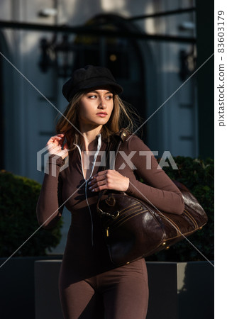 Fashionable young brunette woman with long legs wearing Solid Long Sleeve Bodycon One Piece Jumpsuits posing with a leather brown travel bag 83603179