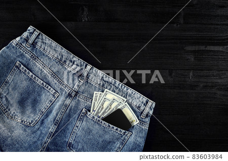 Pocket money. Dollar in hip pocket of worn blue jeans. Close-up. 83603984