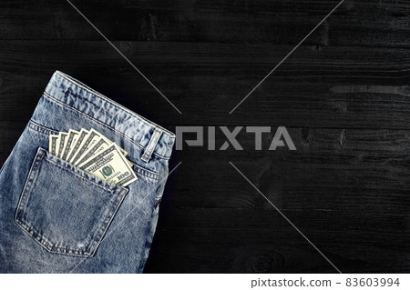 Pocket money. Dollar in hip pocket of worn blue jeans. Close-up. 83603994