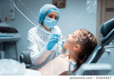 Side view of female dentist who treats teeth of little child patient in dental office. Dentistry Side view of female dentist who treats teeth of little child patient in dental office. Dentistry 83604467