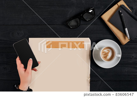 Newspaper and coffee cup, reading glasses, notebook, hands holding smartphone. Newspaper and coffee cup, reading glasses, notebook, hands holding smartphone. 83606547