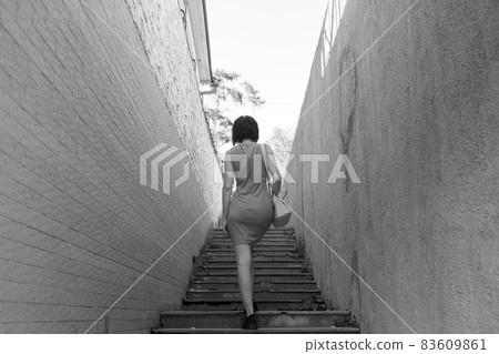 A slender brunette climbs the stairs in a narrow dangerous deserted dark alley 83609861