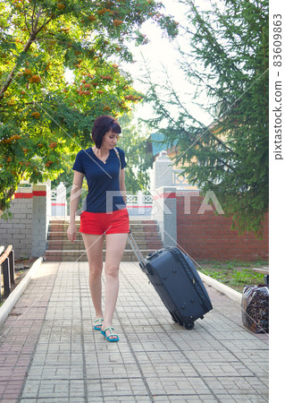 A female tourist with a large heavy suitcase is walking with difficulty through the train station 83609863