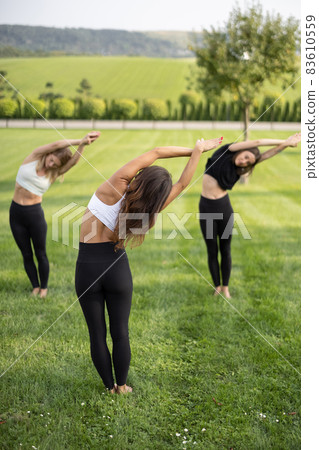 Girls practicing yoga on fitness mats on meadow 83610559