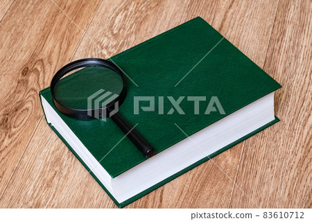 Green cover book and magnifier on wooden table Green cover book and magnifier on wooden table 83610712