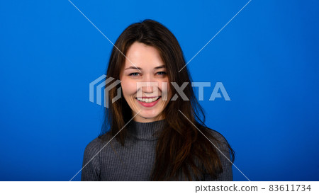 Photo of smiling, cheerful young female in grey dress on blue background 83611734
