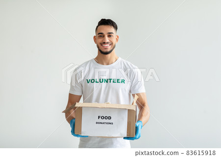 Portrait of young arab man wearing volunteer t-shirt, gloves, holding donations box, standing on light background Portrait of young arab man wearing volunteer t-shirt, gloves, holding donations box, standing on light background 83615918